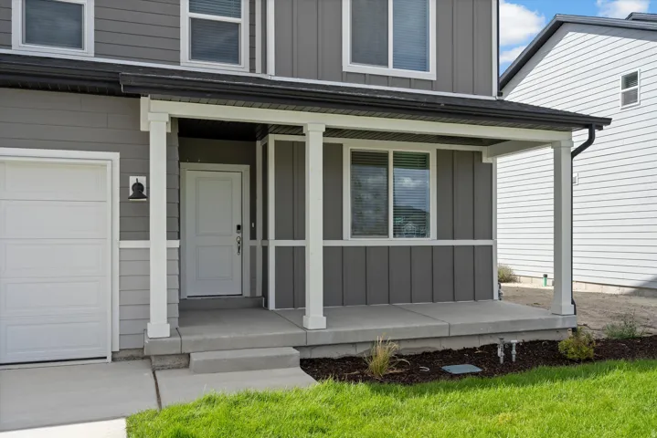 Contemporary exterior featuring gray horizontal and vertical siding, a covered porch with white columns, and a white paneled garage door