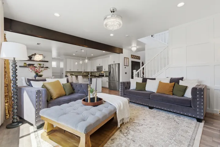 Open-concept living area with wood-finish flooring, a contemporary chandelier, and a prominent staircase featuring white paneling