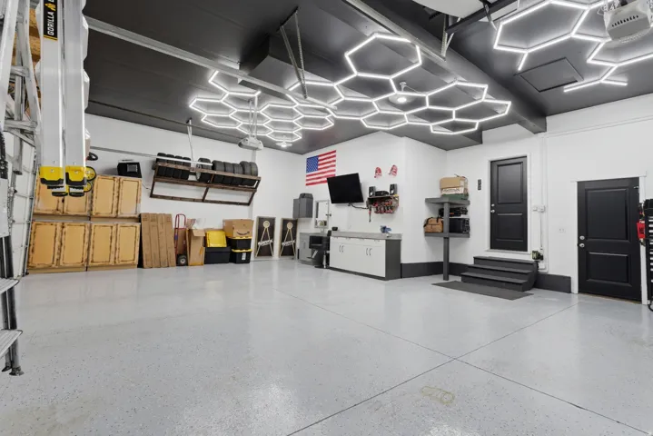 Spacious garage featuring a durable epoxy flooring finish, dark painted ceiling with hexagonal LED lighting, white walls, and built-in cabinetry