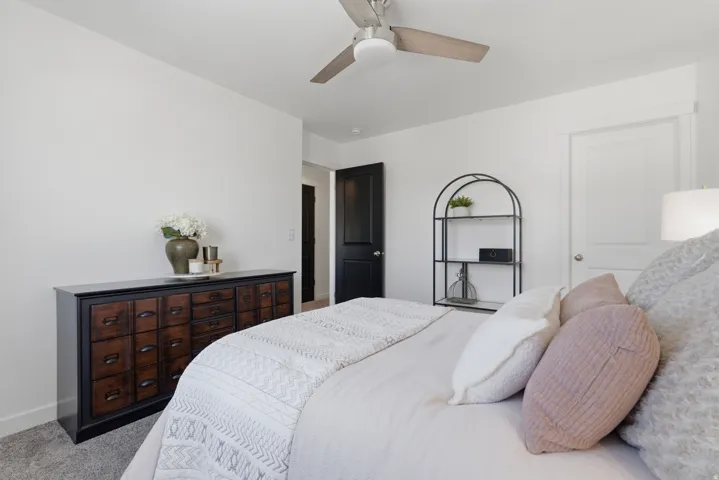 Carpeted room featuring a ceiling fan with light fixture, white walls, and a white interior door