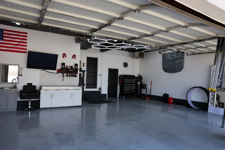 Spacious garage featuring epoxy flooring, built-in cabinetry with a countertop, utility sink with a mirror, and modern overhead lighting