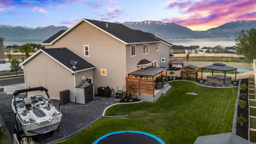 Rear exterior featuring a spacious lawn, covered patio with string lights, and a hot tub beneath a gazebo