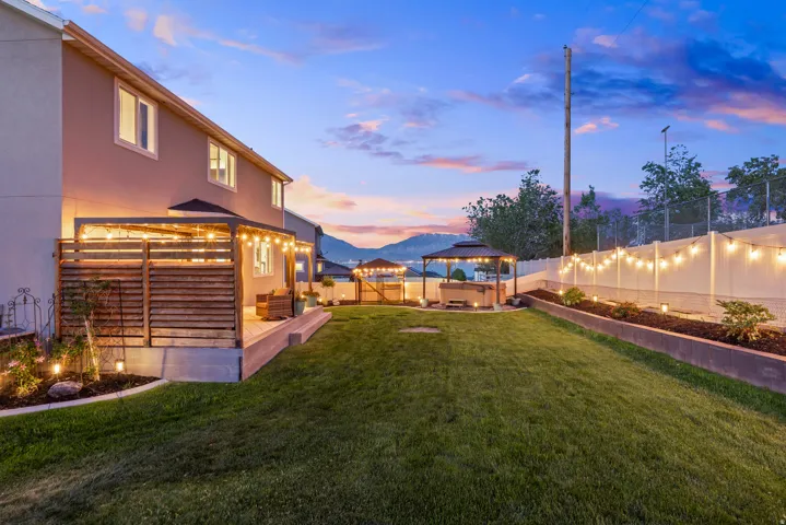 Expansive backyard featuring a manicured lawn, a covered patio with string lighting, and a separate gazebo area