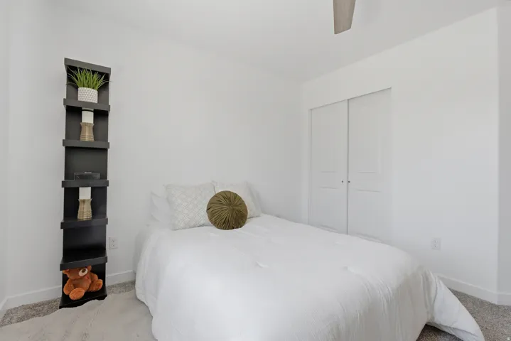 Light-filled room featuring a built-in corner shelving unit, sliding closet doors, ceiling fan, and grey carpet flooring