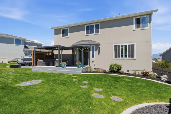 Expansive backyard featuring a lush lawn, stepping stones, and a concrete patio with a dark-framed pergola