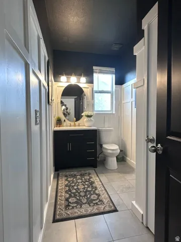 Powder room featuring board and batten wainscoting, a dark vanity with a white countertop, an oval mirror, and a three-light fixture