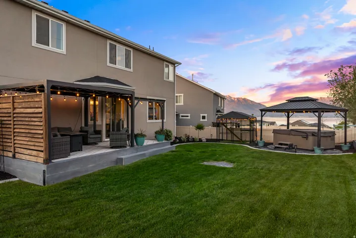 Expansive backyard featuring a manicured lawn, a large entertainment deck with a pergola, and a separate gazebo with a hot tub