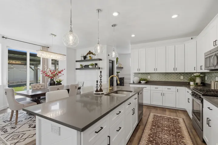 Spacious kitchen featuring a large island with an undermount sink, white cabinetry with black hardware, dark countertops, a herringbone tile backsplash, and stainless steel appliances
