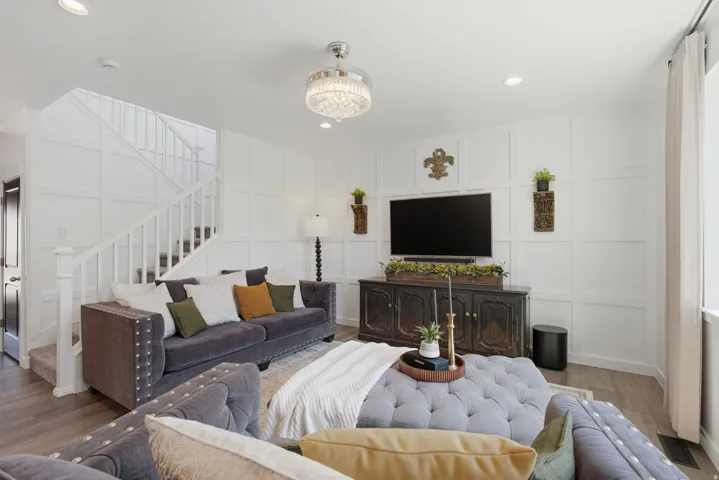 Spacious living area featuring white paneled walls, wood-finish flooring, recessed lighting, and a crystal chandelier