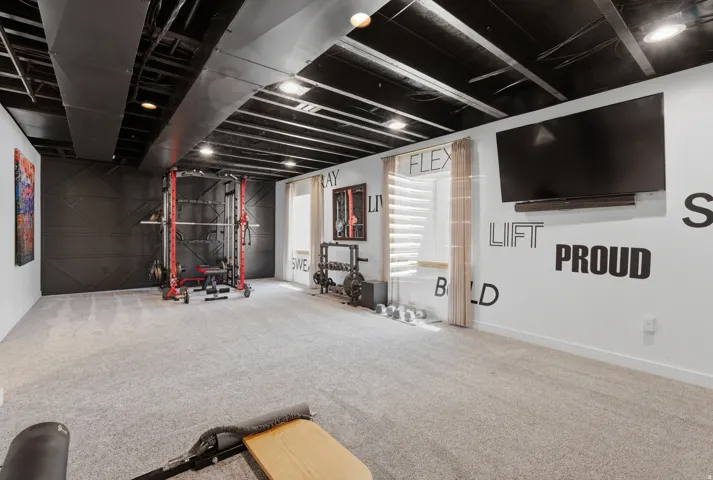 Spacious room featuring light gray carpet flooring, white walls, and a black painted exposed ceiling with recessed lighting