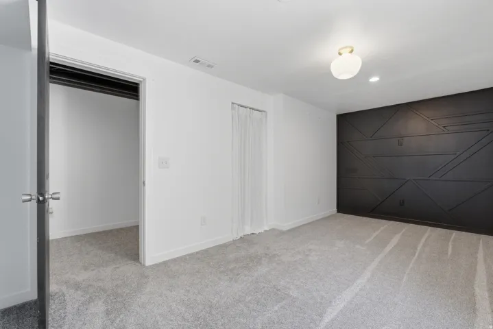 Spacious room featuring a dark accent wall with geometric paneling, light gray carpeting, and a semi-flush mount ceiling fixture