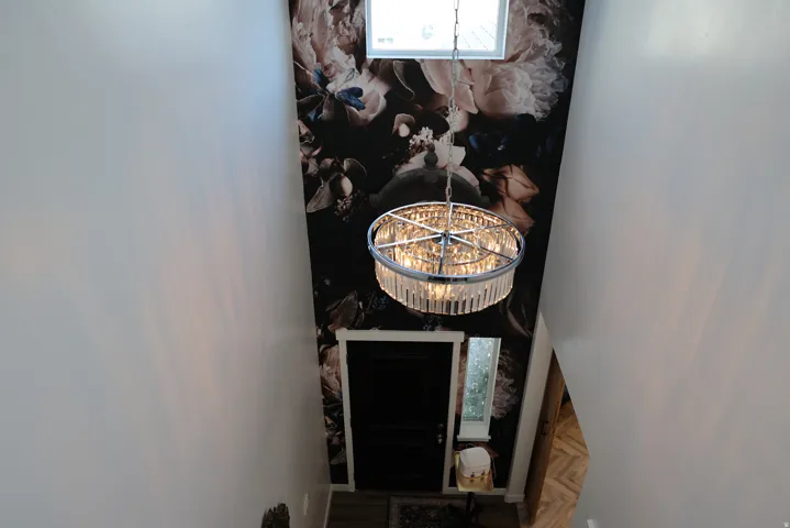 Foyer featuring a decorative crystal chandelier, a dark floral accent wall, a transom window, and a dark entry door with sidelight