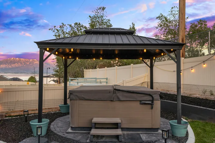Covered outdoor spa area featuring a metal gazebo, string lighting, and a composite spa with steps
