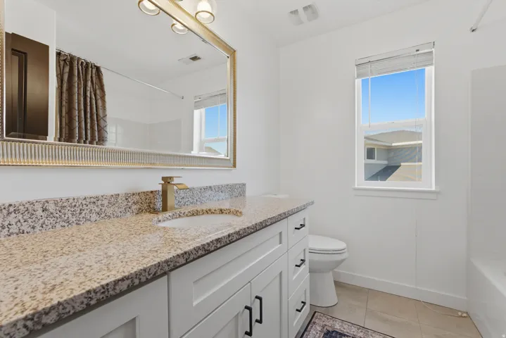 Bathroom featuring a wide vanity with a speckled countertop, a gold-toned faucet, and a large framed mirror