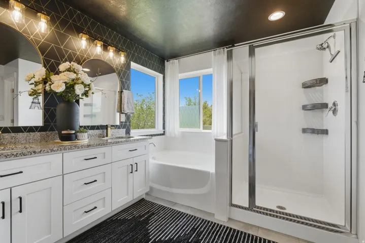 Contemporary bathroom featuring a double vanity with stone countertops, a soaking tub, and a separate glass-enclosed shower