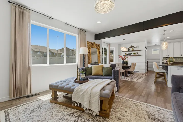 Open concept living space featuring wood-finish flooring, a decorative ceiling beam, and a large multi-pane window with neutral drapes