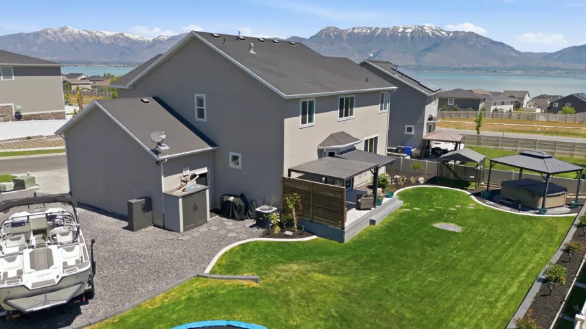 Expansive backyard featuring a manicured lawn, gravel patio areas, a covered pergola, and a separate structure housing a hot tub