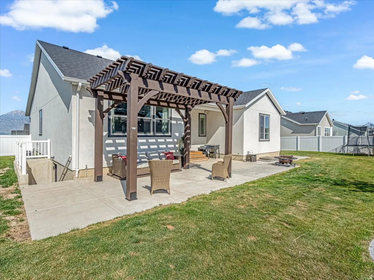 Spacious concrete patio featuring a dark wood-finish pergola, a built-in fire pit, and a full white vinyl perimeter fence