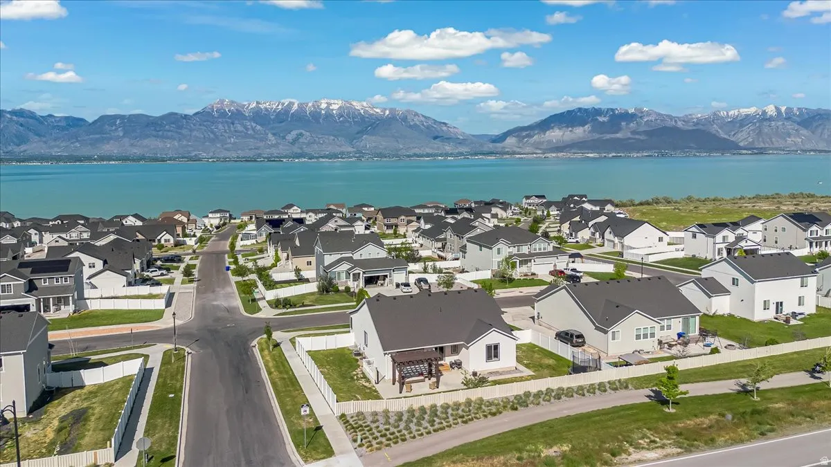Residential development featuring a grid of paved streets and sidewalks, individual homes with dark-pitched roofs, and a prominent water body in the background