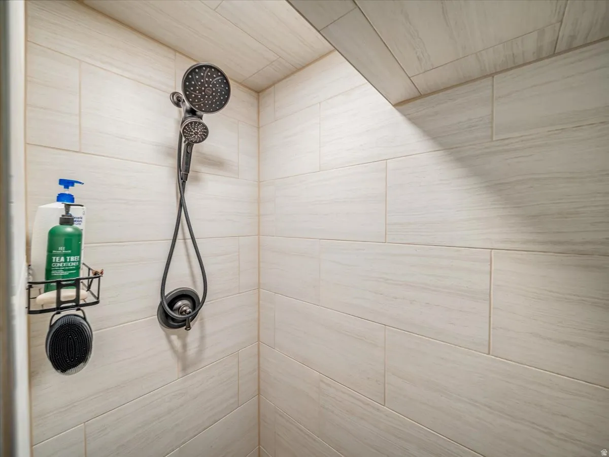 Shower enclosure featuring light-toned rectangular tile walls and a multi-function shower head with a handheld sprayer