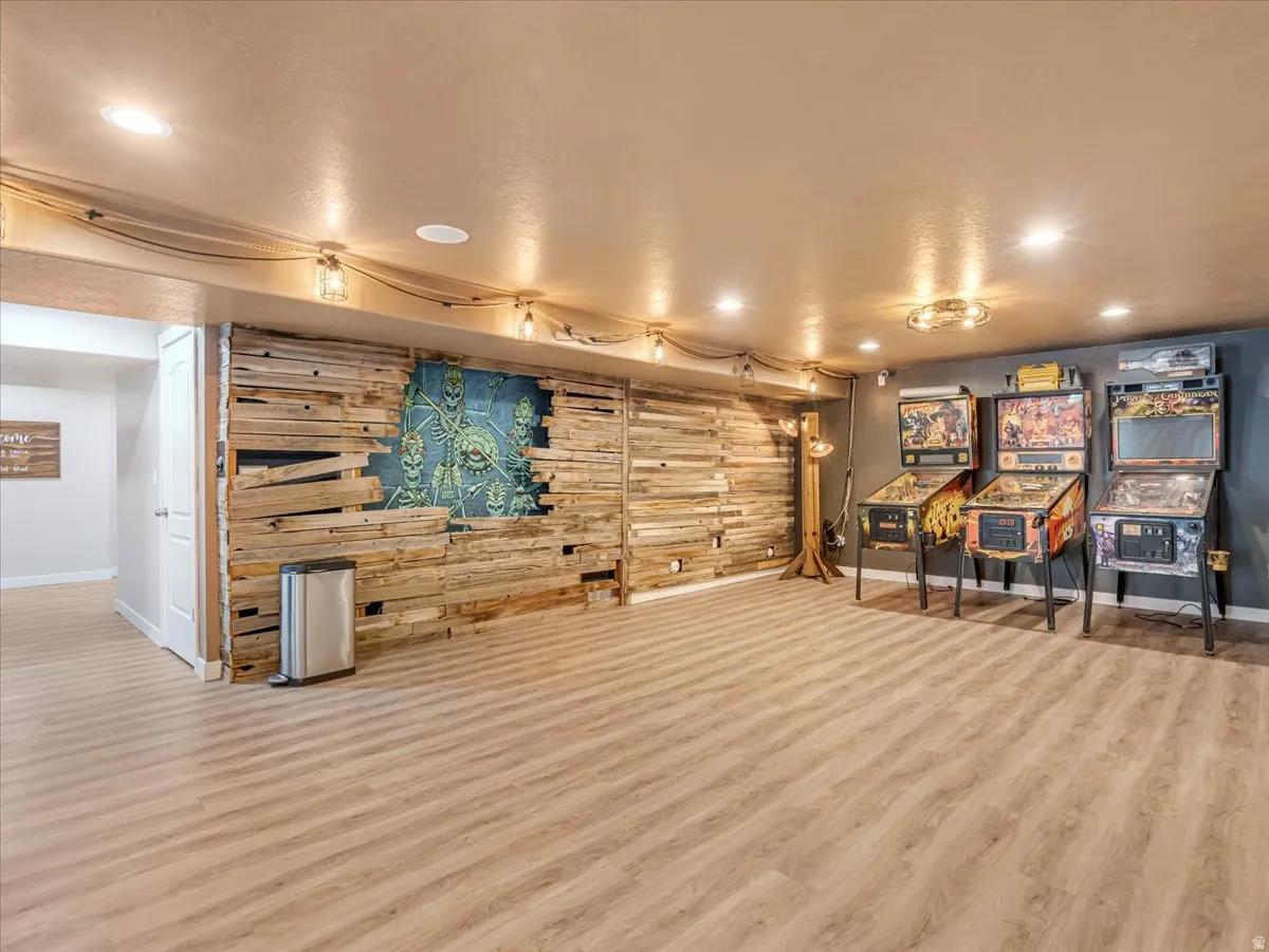 Spacious recreation room featuring wood-finish flooring, a decorative accent wall with wood paneling, recessed lighting, and modern industrial-style light fixtures