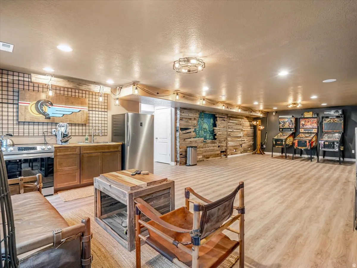 Spacious entertainment area featuring wood-finish flooring, a built-in kitchenette with stainless steel appliances, and a wall of reclaimed wood paneling