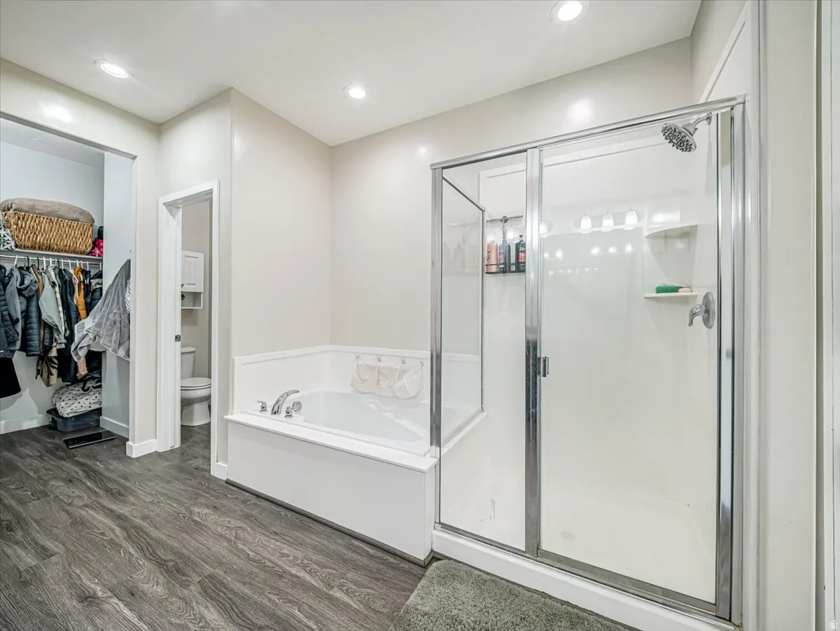 Bathroom featuring a white soaking tub, a separate glass-enclosed shower with a multi-setting showerhead, recessed lighting, and wood-finish flooring