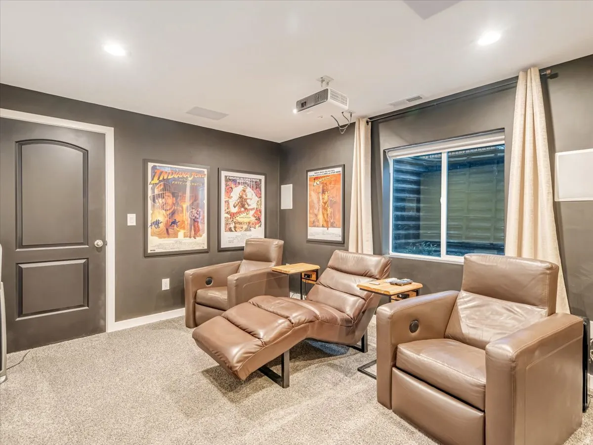 Carpeted room featuring a projector, recessed lighting, and a window with a valance