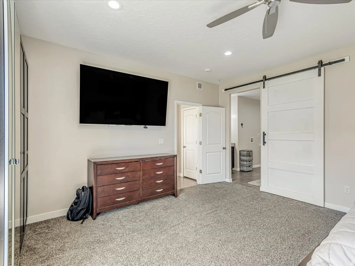 Plush grey carpeting and neutral wall tones complement modern recessed lighting and a ceiling fan