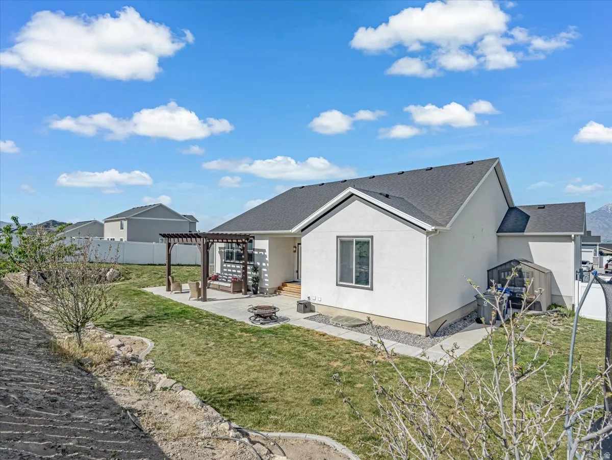 Rear exterior featuring a stone-paved patio with a pergola, a manicured lawn, and a gravel perimeter