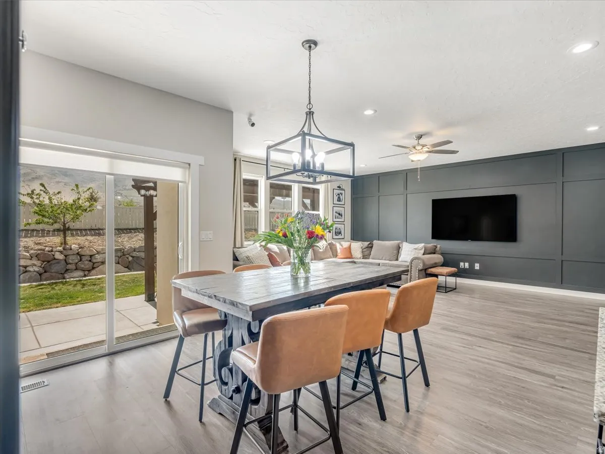 Open-concept living area featuring wood-finish flooring, a contemporary dining island with seating, and a living room with a paneled accent wall