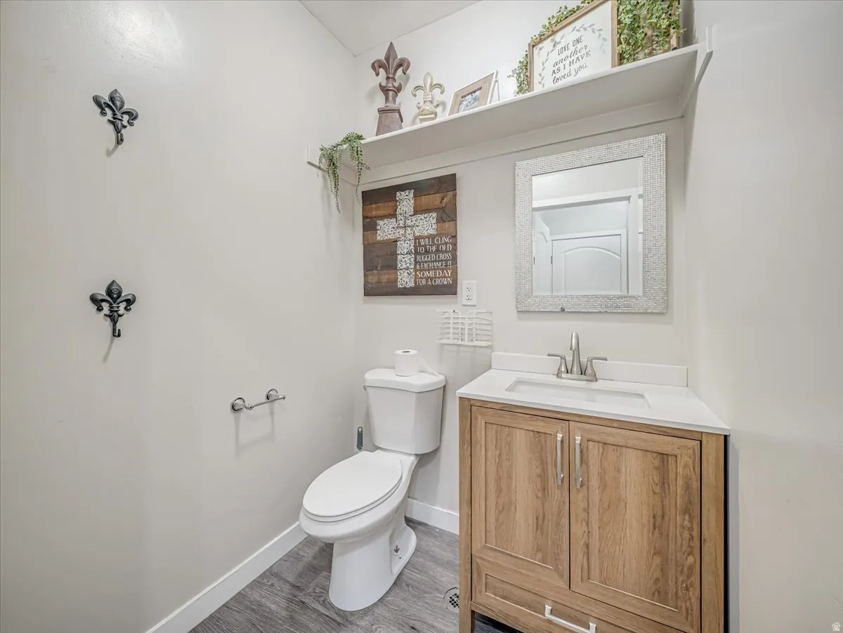 Bathroom featuring a wood-finish vanity with a white countertop and basin sink, a wall-mounted mirror, a toilet, and wood-look flooring