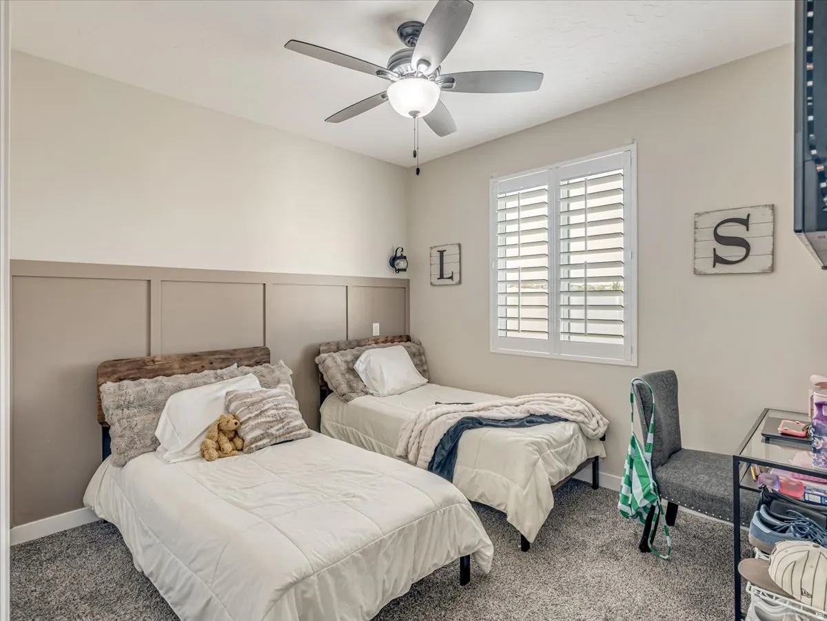 Carpeted room featuring a ceiling fan, a window with white plantation shutters, and a two-tone wall with lower paneling