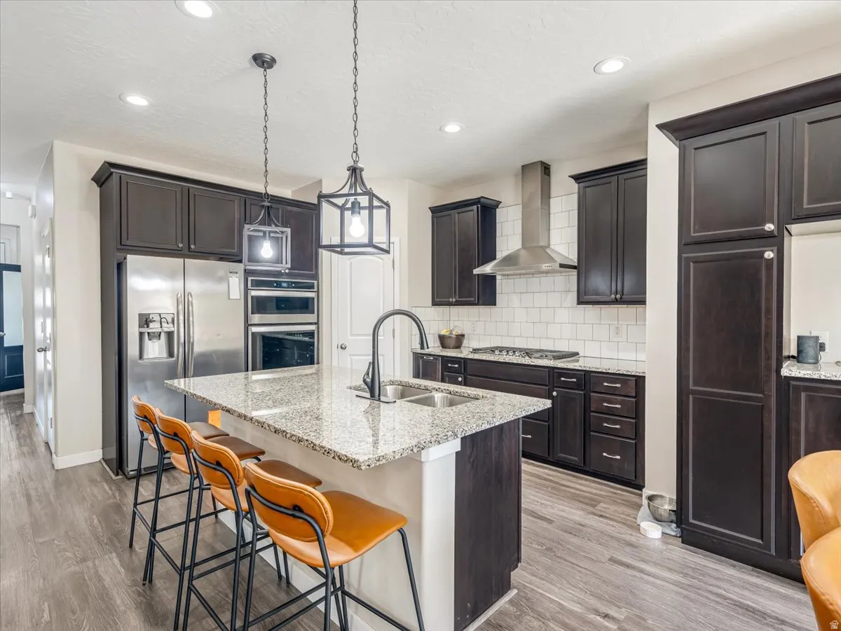 Kitchen featuring granite countertops, wood-finish flooring, dark wood cabinetry, stainless steel appliances, and subway tile backsplash