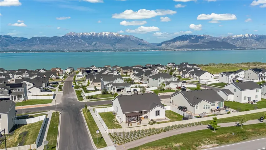 Residential development featuring a grid of paved streets and sidewalks, individual homes with dark-pitched roofs, and a prominent water body in the background
