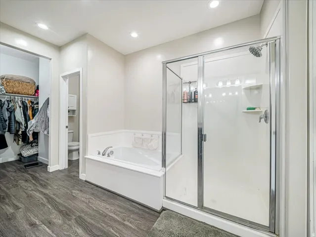 Bathroom featuring a white soaking tub, a separate glass-enclosed shower with a multi-setting showerhead, recessed lighting, and wood-finish flooring