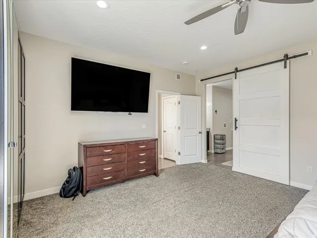 Plush grey carpeting and neutral wall tones complement modern recessed lighting and a ceiling fan