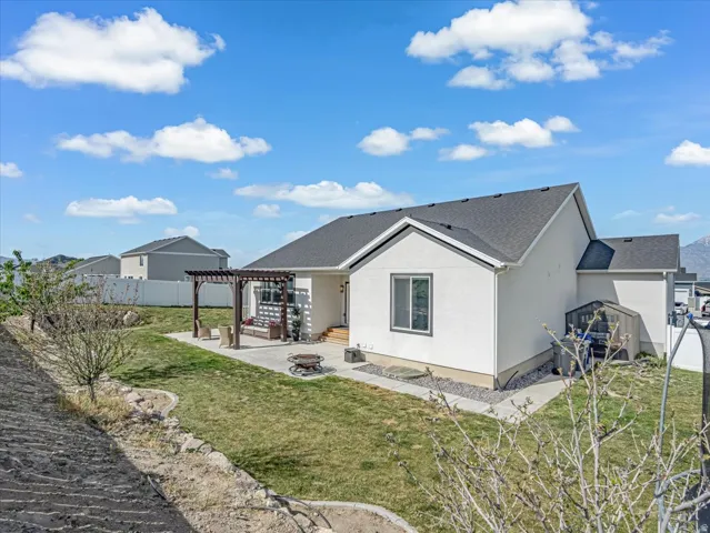 Rear exterior featuring a stone-paved patio with a pergola, a manicured lawn, and a gravel perimeter