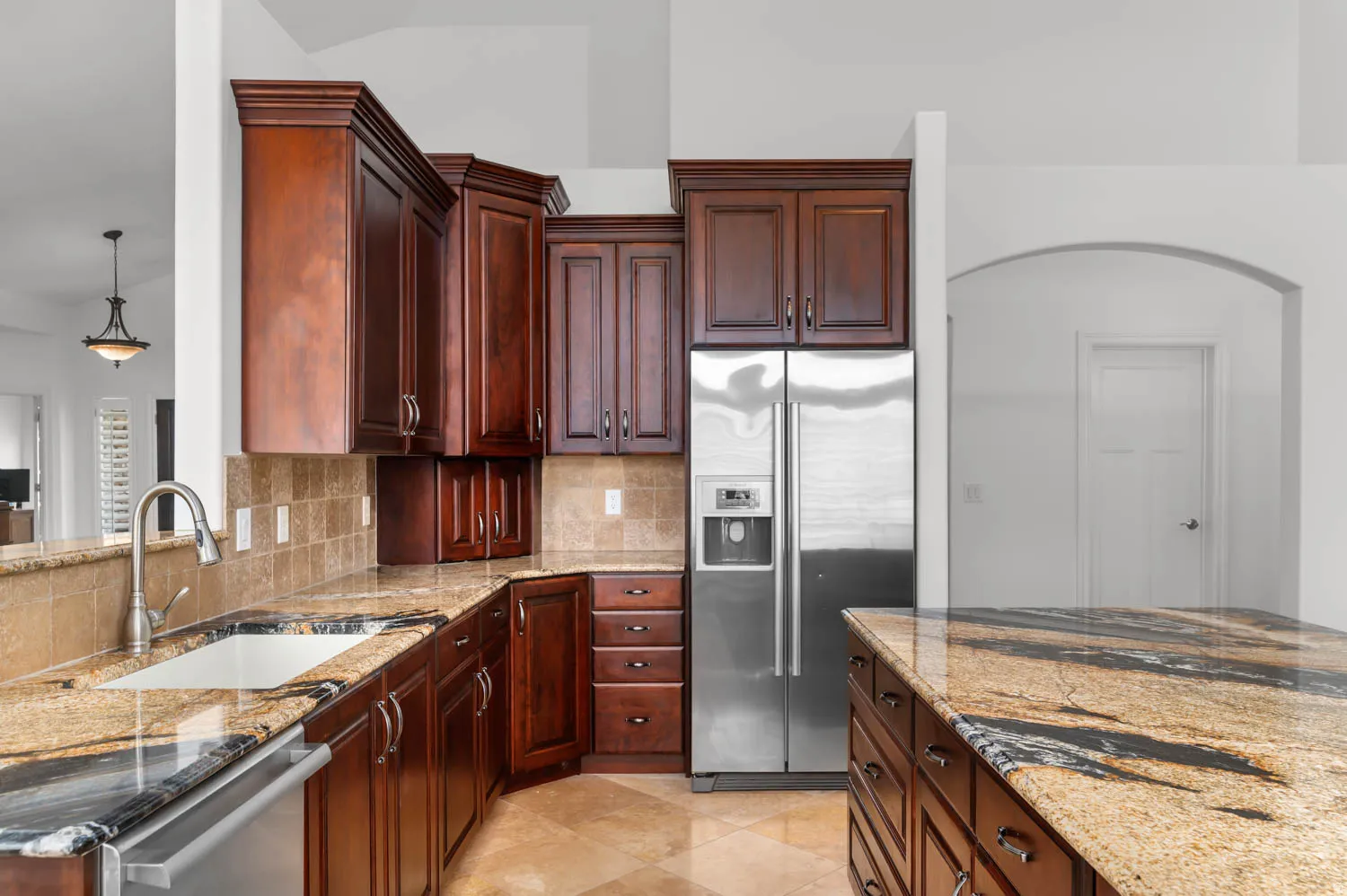 Kitchen featuring rich wood cabinetry, patterned stone countertops, stainless steel appliances, a tile backsplash, and an undermount sink with a gooseneck faucet