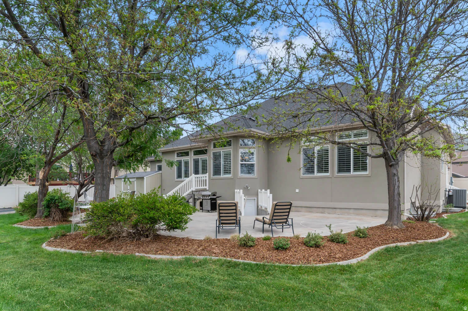 Expansive backyard featuring a stone patio, mature trees, and manicured lawn