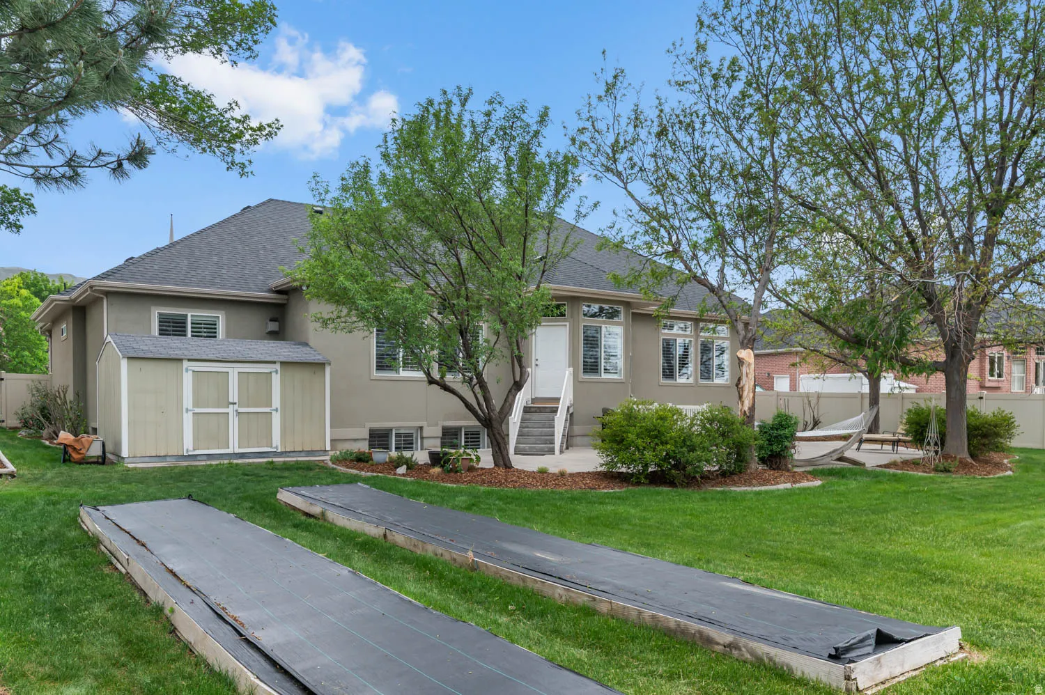 Expansive backyard featuring a manicured lawn, established trees, and a concrete patio