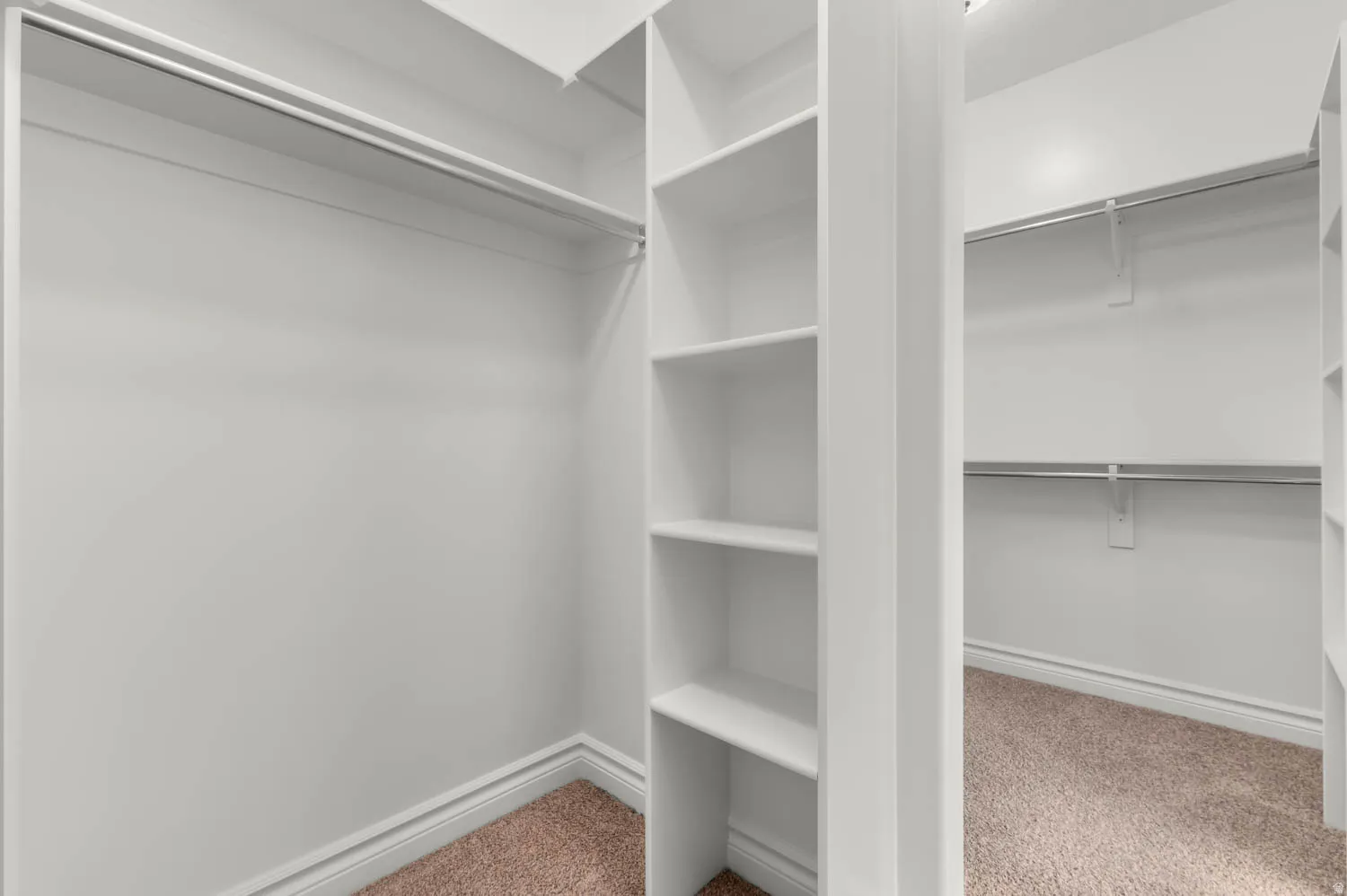 Walk-in closet featuring white built-in shelving, white baseboards, and neutral-toned carpeting