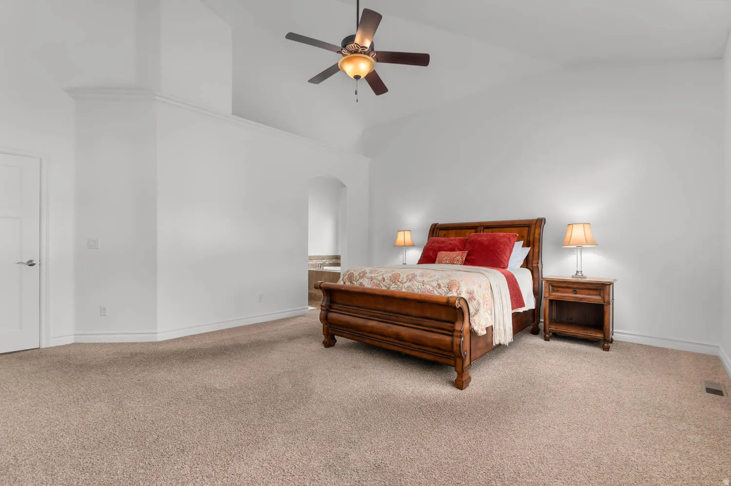 Expansive carpeted room featuring a ceiling fan with integrated lighting, vaulted ceilings, and white trim