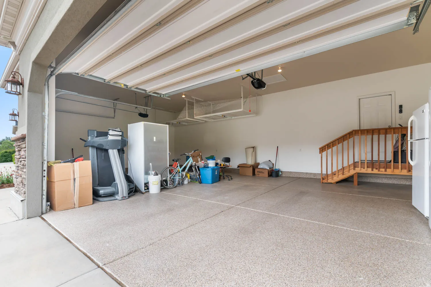 Spacious garage featuring a durable epoxy-coated floor, integrated lighting, and direct interior access via a wooden staircase