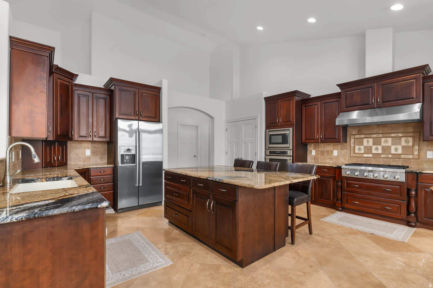 Gourmet kitchen featuring rich wood cabinetry, granite countertops, a large center island with seating, stainless steel appliances, and tile flooring