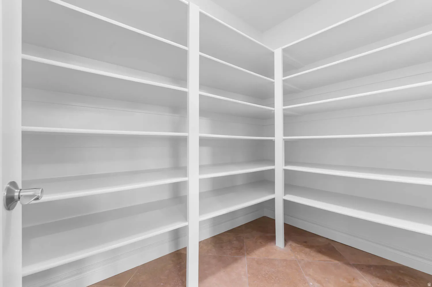 Spacious walk-in pantry featuring extensive white shelving, tile flooring, and a contemporary doorknob