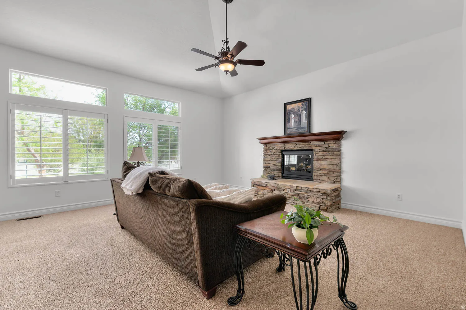 Spacious living area featuring a stone-clad fireplace with a wood mantel, high vaulted ceilings, and a ceiling fan