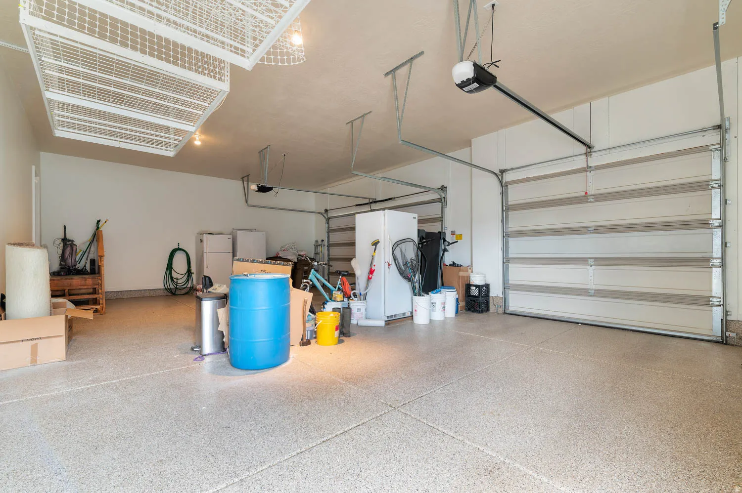 Spacious garage featuring a durable epoxy-coated floor, two overhead garage doors, overhead storage racks, and an automatic garage door opener