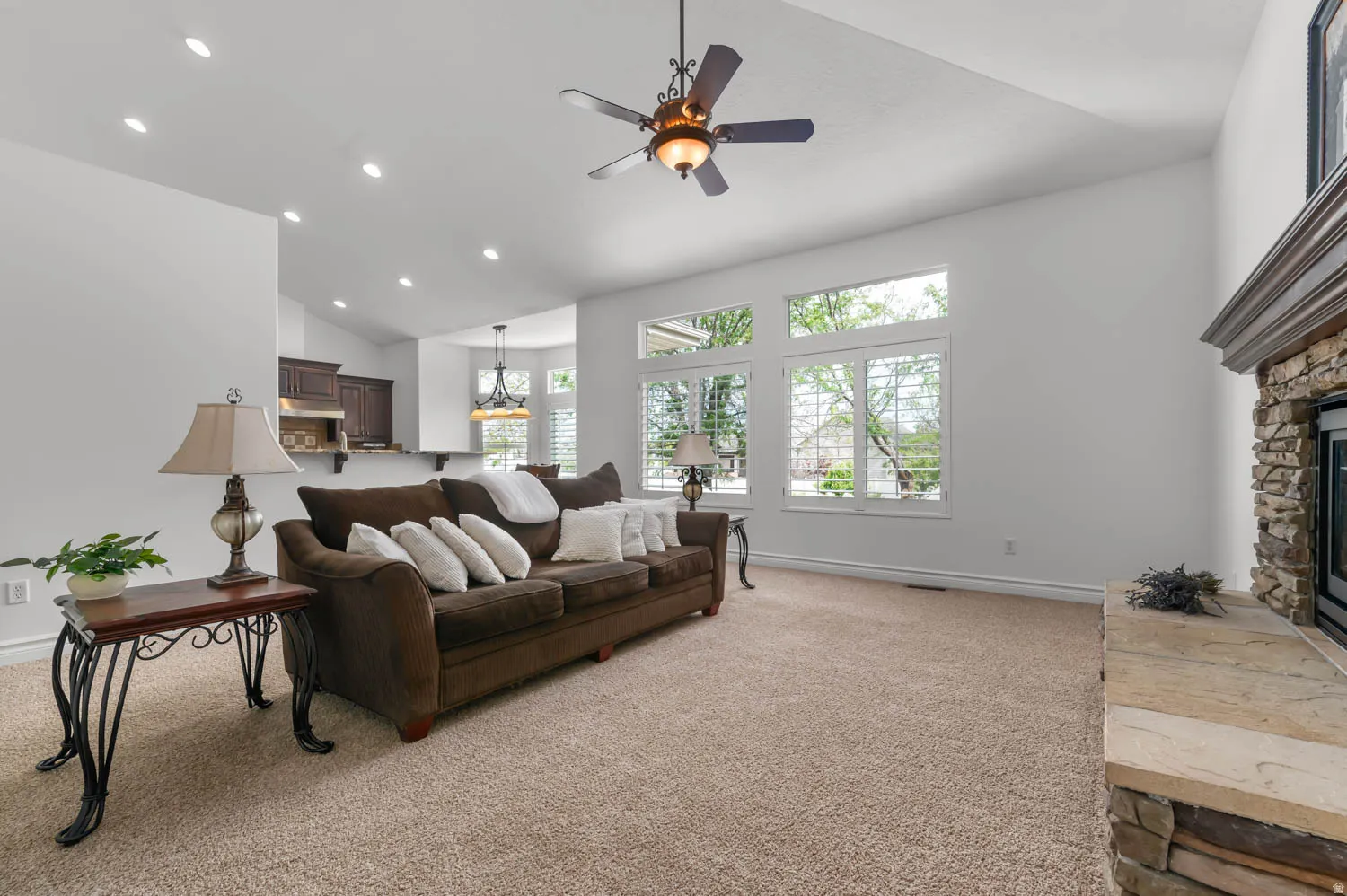 Vaulted ceiling living room featuring a stone-clad fireplace with a stone hearth, recessed lighting, and a ceiling fan