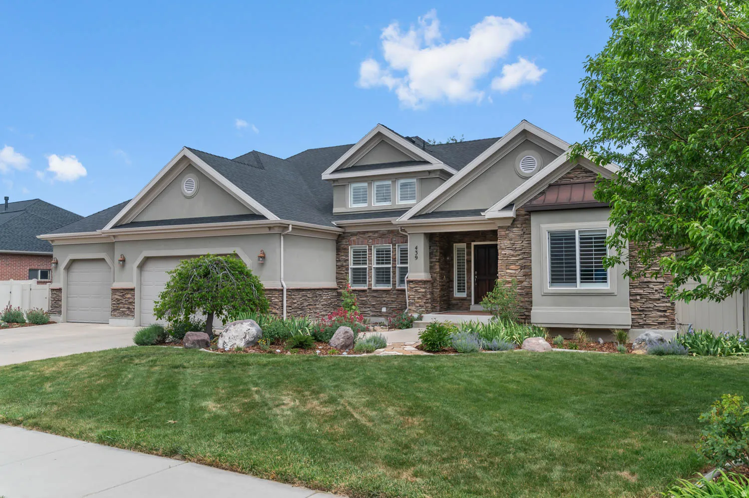 Stucco and stone facade with a two-car garage, mature landscaping, and an inviting entryway